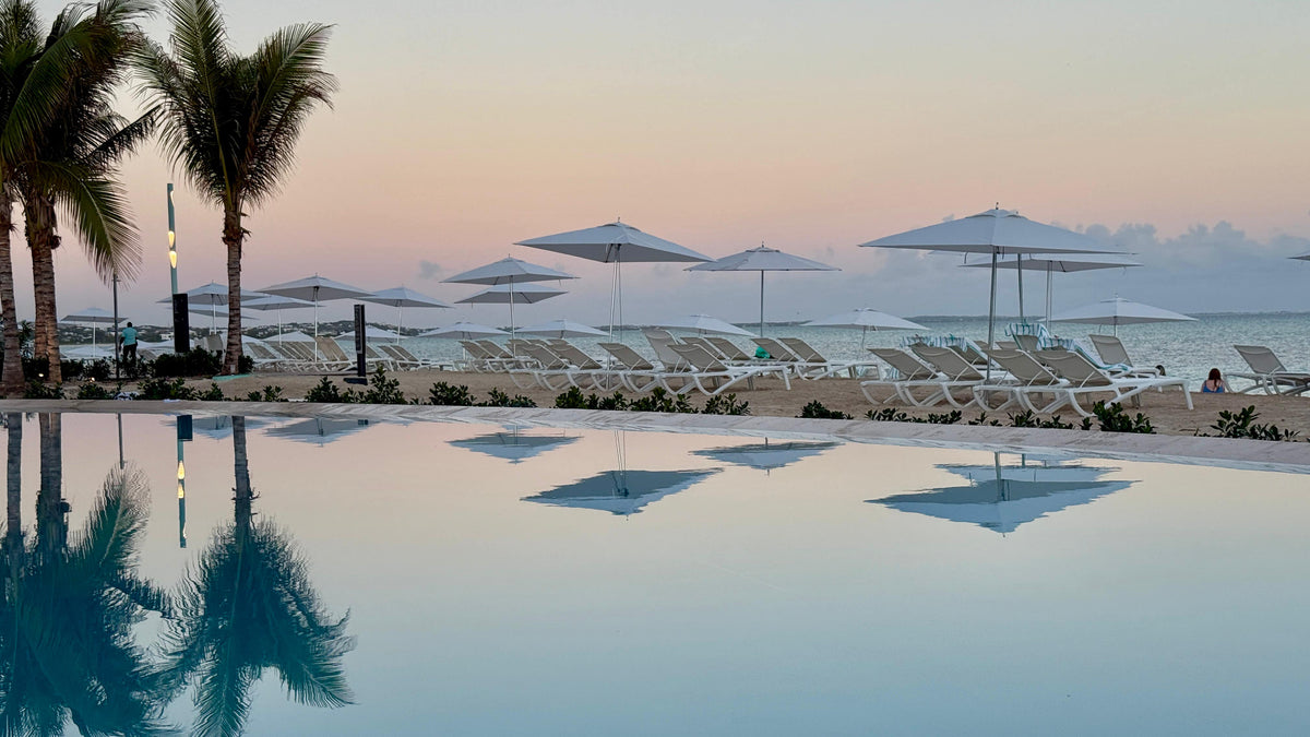 Palm trees and beach umbrellas beside a resort infinity pool at sunset